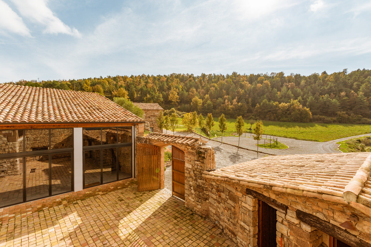 Tiled rooftops and the courtyard gate with wooded Catalan hills beyond
